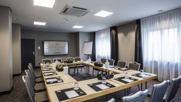 Un salón de conferencias con una larga mesa, sillas, una pantalla de proyector y una pizarra.