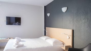 A hotel room with a bed, a TV, a desk with a book, and a chair.