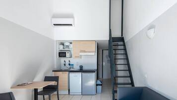 A compact kitchen with a microwave, sink, and dishwasher, a dining area with a table and chairs, and a staircase leading to an upper level.