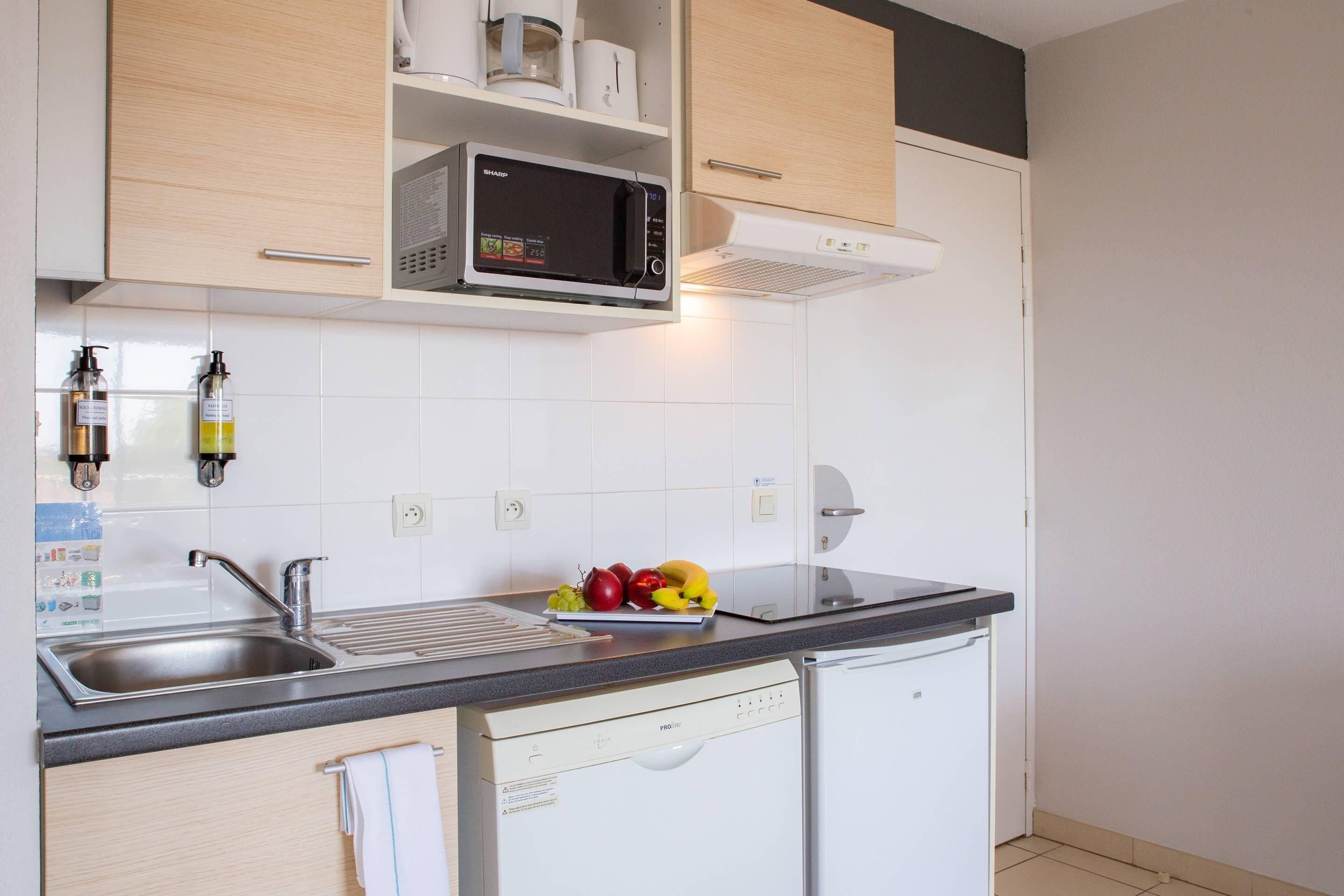 Una cocina con microondas, pileta y escurreplatos.