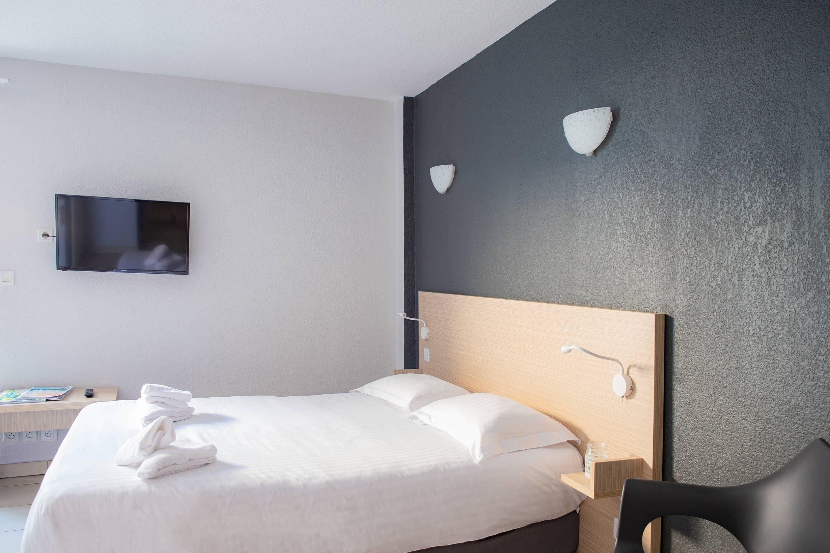 Ein Hotelzimmer mit einem Bett, einem Fernseher, einem Schreibtisch mit einem Buch und einem Stuhl.