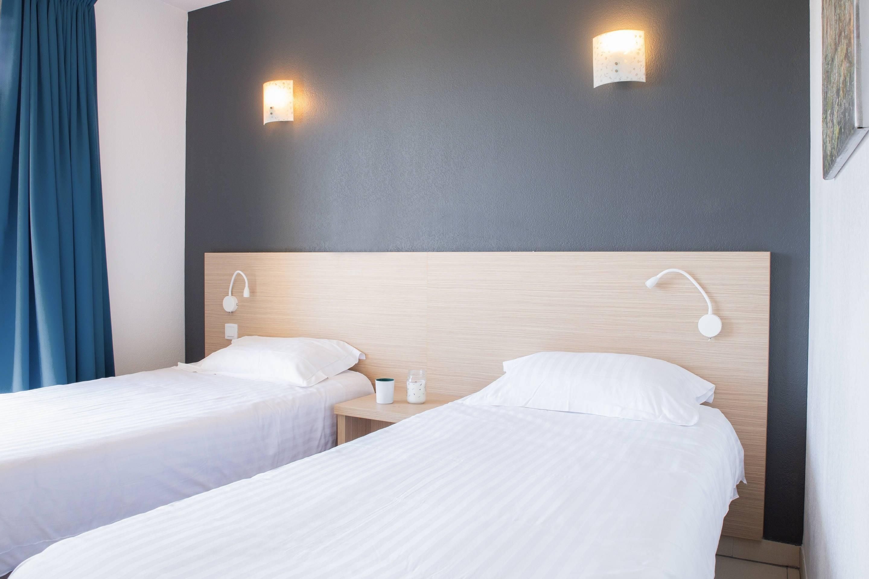 Ein Hotelzimmer mit zwei Einzelbetten, einem Holz-Kopfteil, Nachttischlampen und einem Nachttisch mit Tasse und Glas.