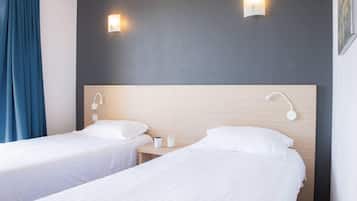 Ein Hotelzimmer mit zwei Einzelbetten, einem Holz-Kopfteil, Nachttischlampen und einem Nachttisch mit Tasse und Glas.