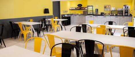 A restaurant with yellow and black chairs, white tables, and a counter with food display.