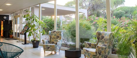 A spacious indoor area with large windows, modern chairs, and potted plants.