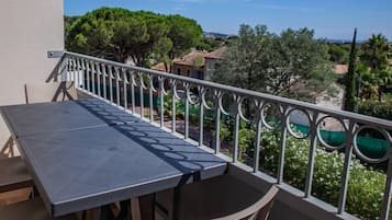 Un balcone con tavolo e sedie, vista su una zona residenziale con alberi e case.