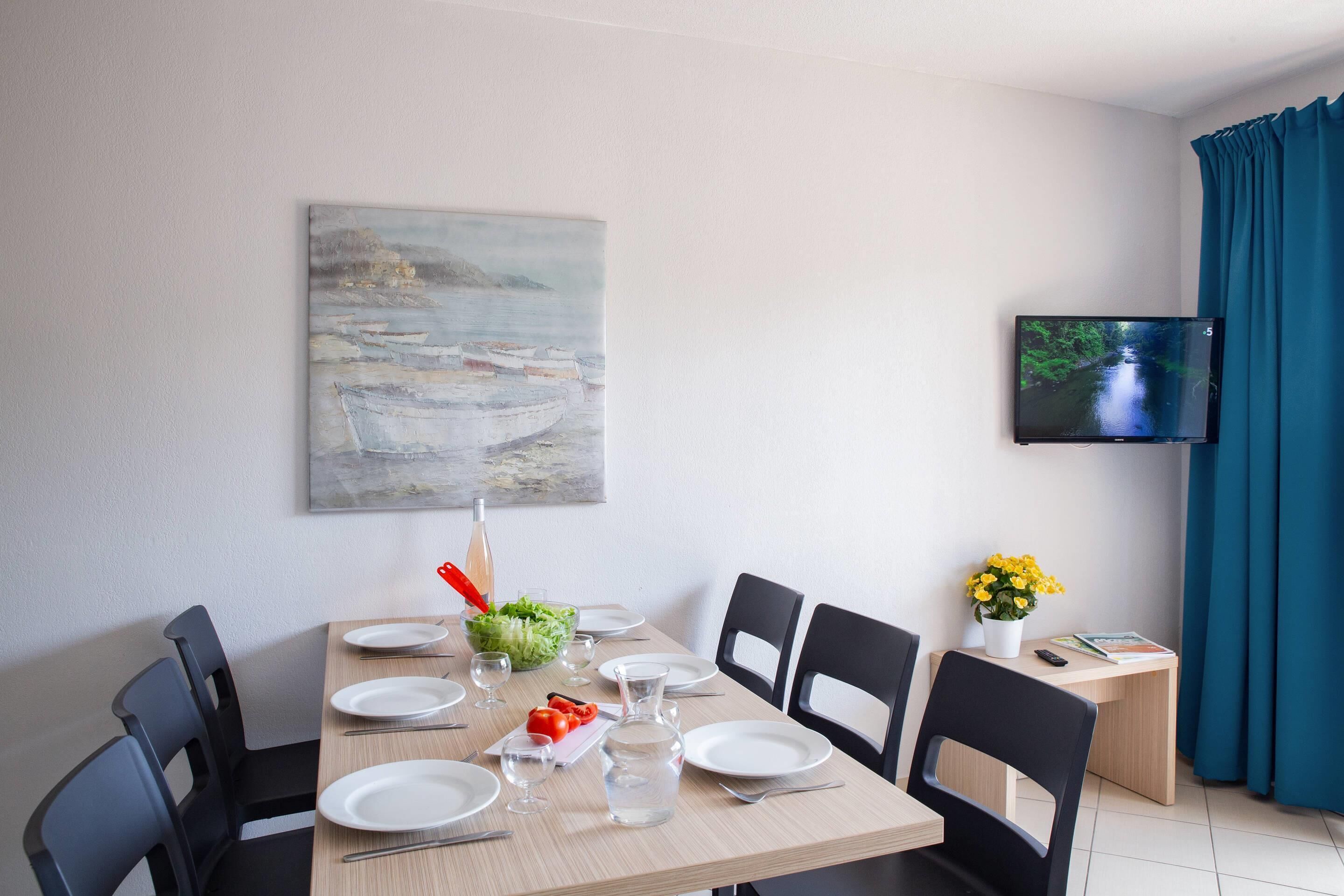 Een eethoek met een tafel voor vier personen, een schilderij aan de muur en een televisie.