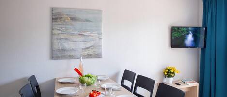 Een eethoek met een tafel voor vier personen, een schilderij aan de muur en een televisie.