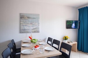Un comedor con una mesa dispuesta para cuatro personas, un cuadro en la pared y un televisor.