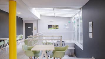 Un intérieur moderne avec un pilier jaune, des chaises vertes, une table blanche et une vue sur un jardin à travers un mur de verre.