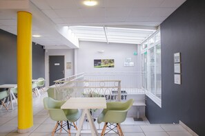 Un interior moderno con un pilar amarillo, sillas verdes, una mesa blanca y vistas a un jardín a través de un muro de cristal.