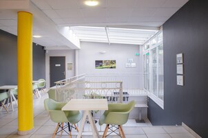 A modern interior with a yellow pillar, green chairs, a white table, and a view of a garden through a glass wall.