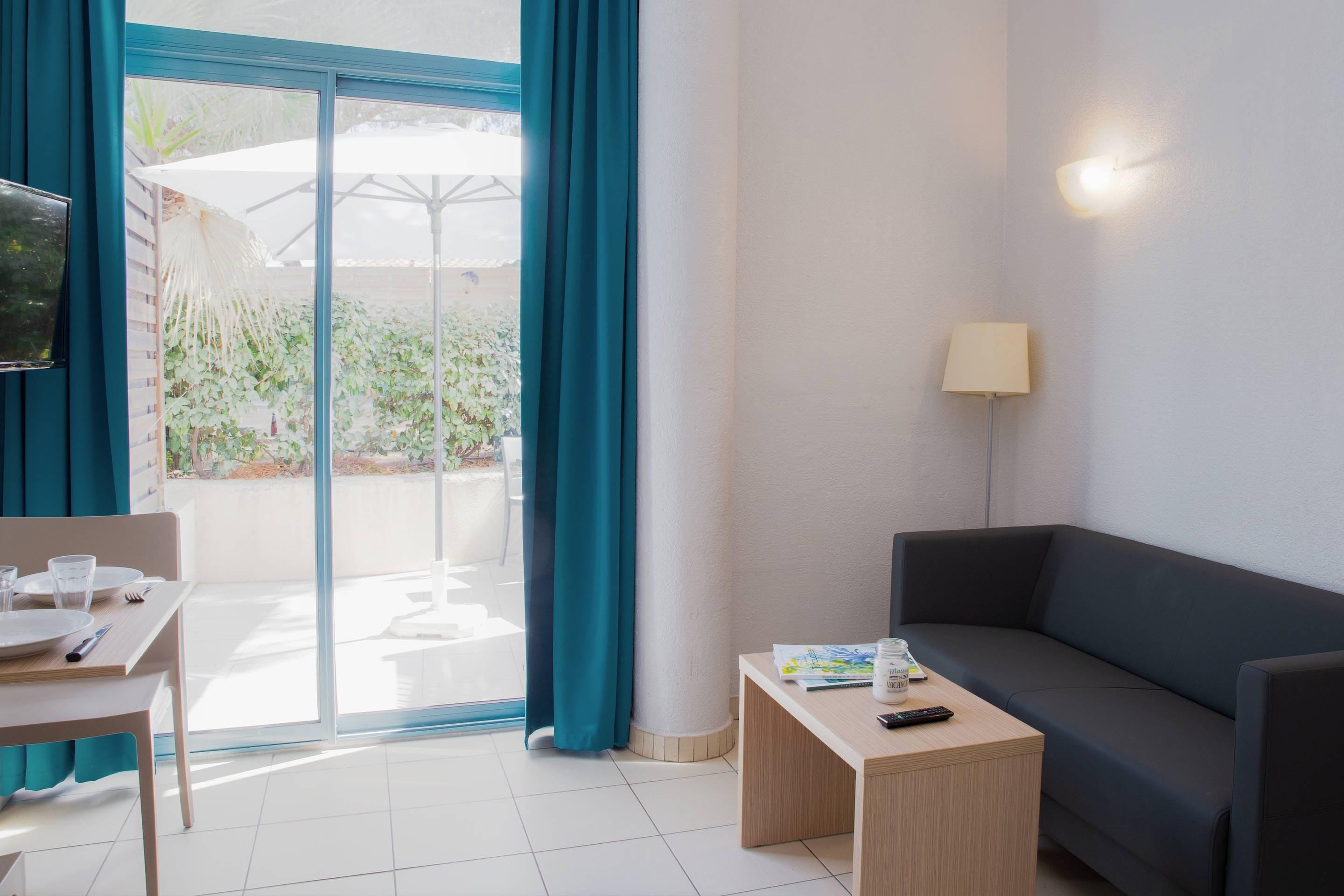 A hotel room with a sofa, a small table, a TV, and a sliding glass door leading to an outdoor area with a patio umbrella.