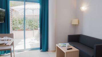 A hotel room with a sofa, a small table, a TV, and a sliding glass door leading to an outdoor area with a patio umbrella.