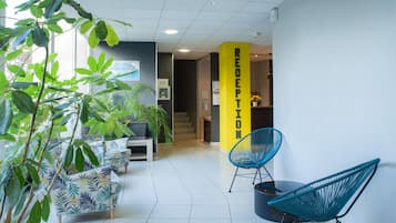A reception area with a yellow pillar labeled 'RECEPTION,' a blue chair, and a sofa with a tropical leaf pattern.