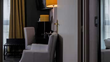 Une chambre d’hôtel avec un fauteuil blanc, une petite table, une lampe et un téléviseur posé sur un meuble.