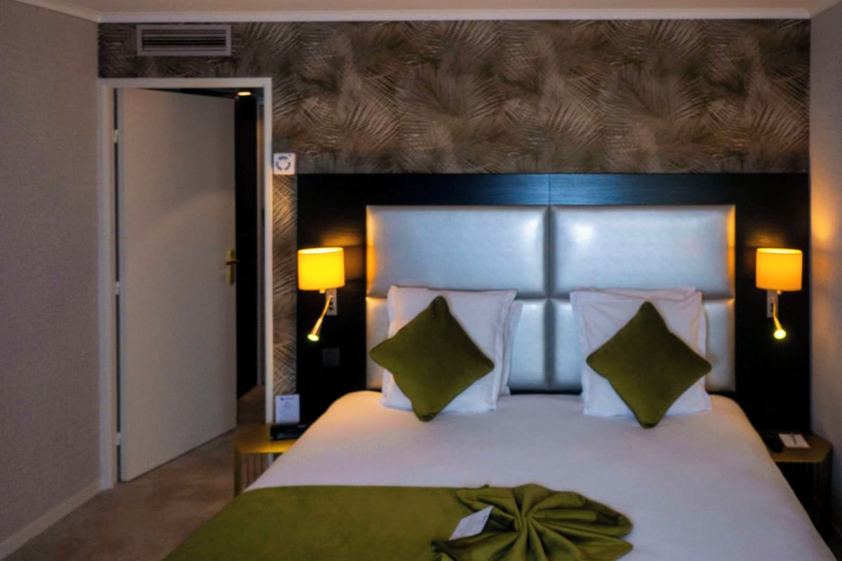 A hotel room with a large bed, two bedside lamps, and a headboard with a leaf pattern.