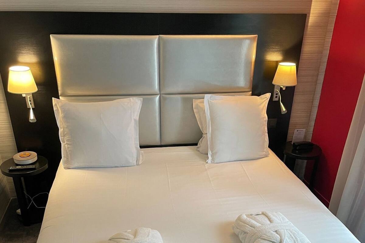 A hotel room with a large bed, two bedside lamps, and two towels on the bed.