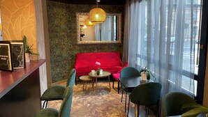 A cozy interior with a red sofa, green chairs, a small round table, and a mirror on the wall.
