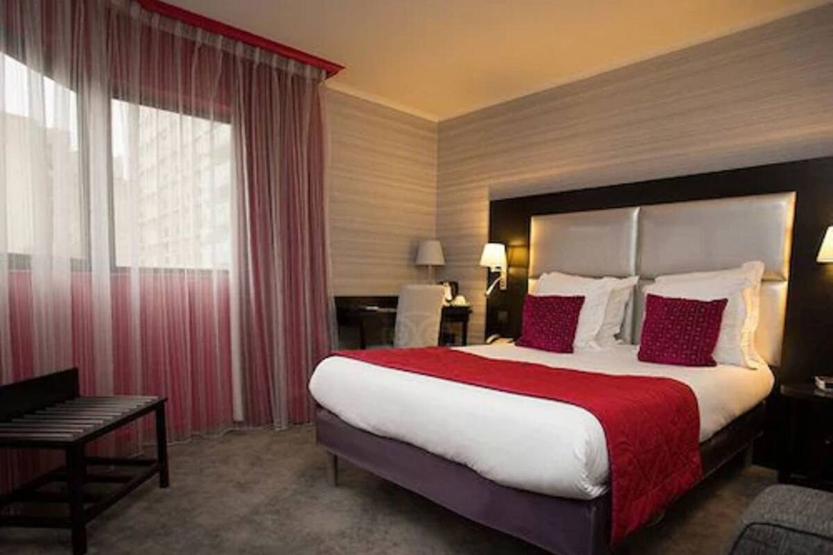 A hotel room with a bed, a desk, a chair, and a window with curtains.