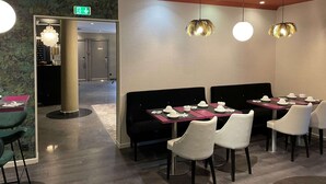 A restaurant with black and white upholstered booths, round tables, and pendant lighting.