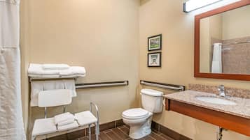A bathroom with a toilet, a sink, a mirror, a shower curtain, and a chair with towels.