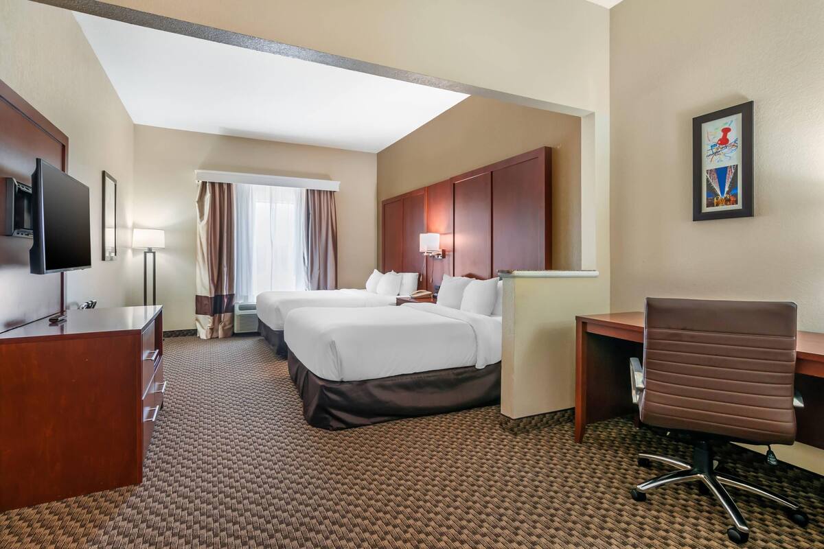 A hotel room with two beds, a desk, a chair, a TV, and a framed picture on the wall.