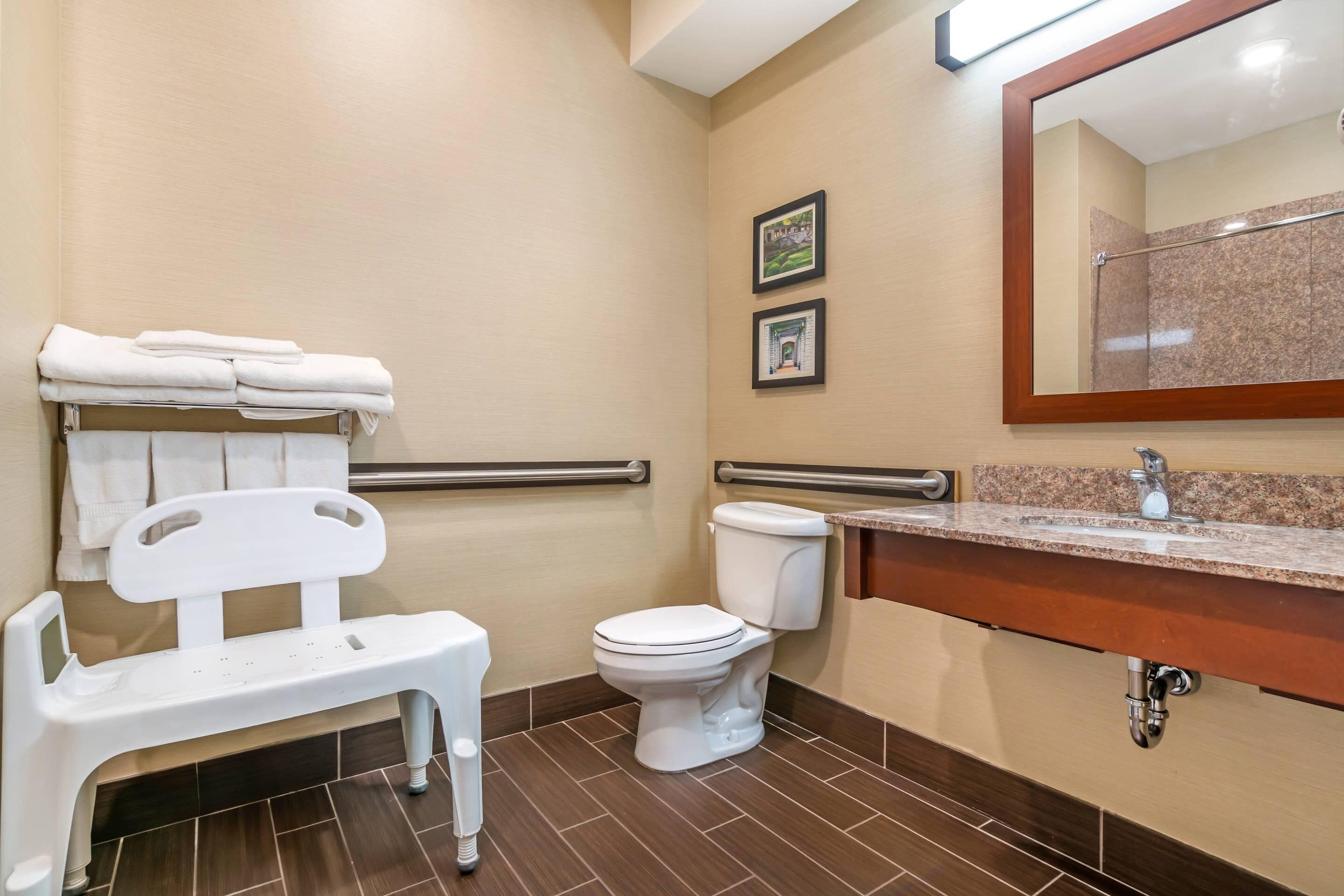 A bathroom with a white bench, a toilet, a sink with a mirror, and two framed pictures on the wall.
