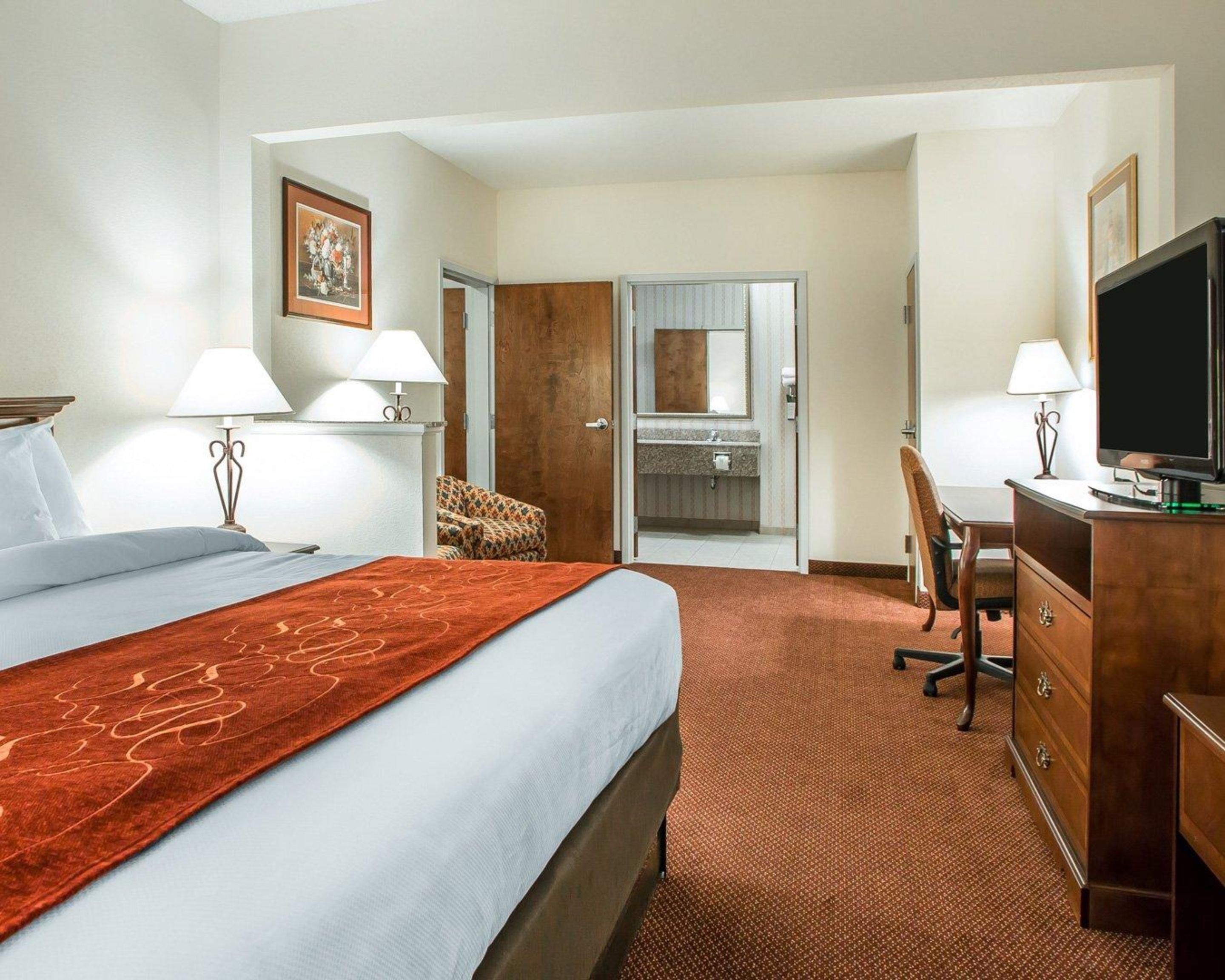 A hotel room with a large bed, a desk, a television, and a bathroom visible through an open door.