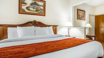 Ein Hotelzimmer mit einem großen Bett, einem hölzernen Kopfteil, weißer Bettwäsche, einer roten Tagesdecke, einem Nachttisch mit Lampe und einem gerahmten Bild an der Wand.