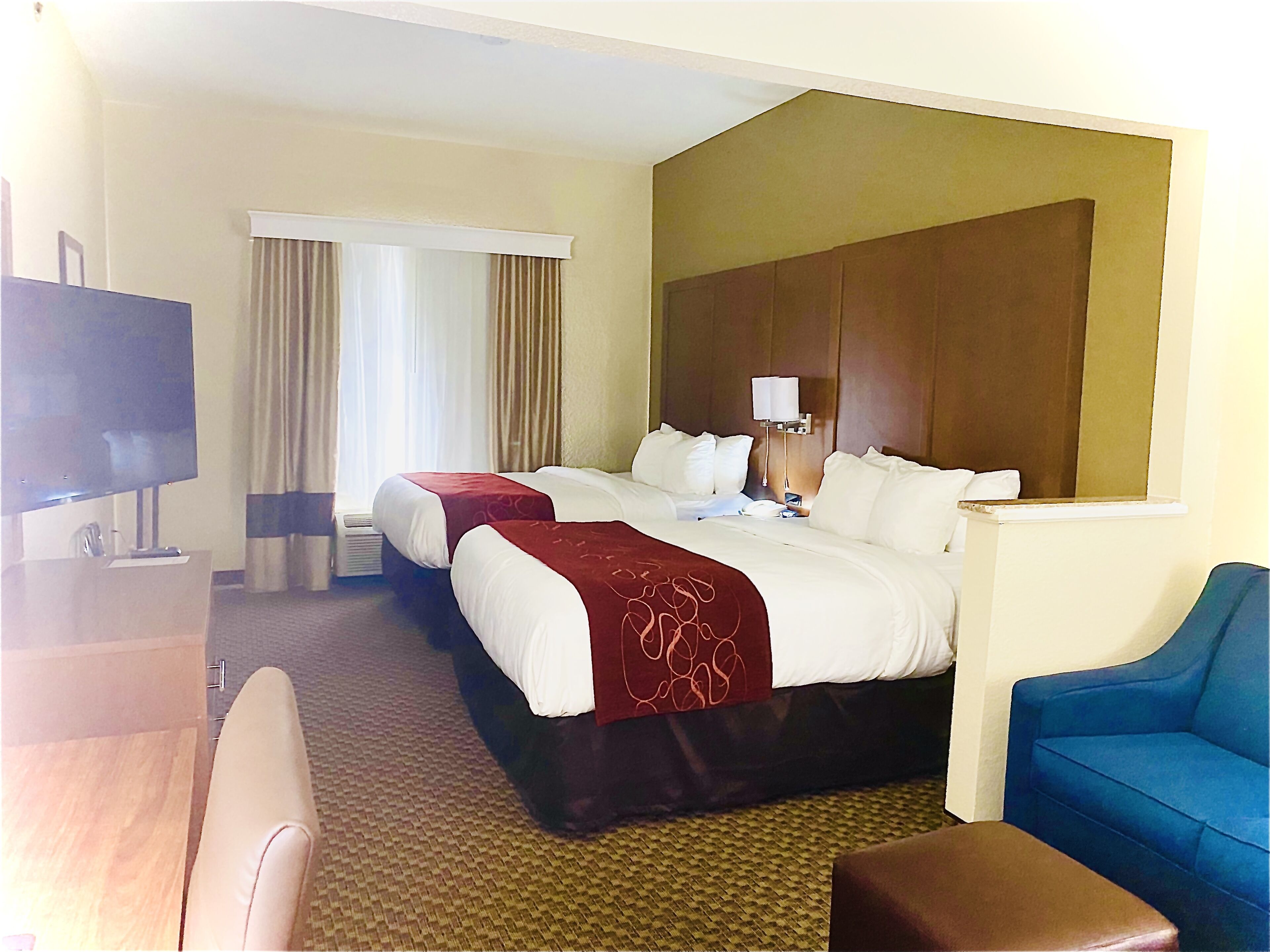 A hotel room with two beds, a TV, a desk, and a blue armchair.