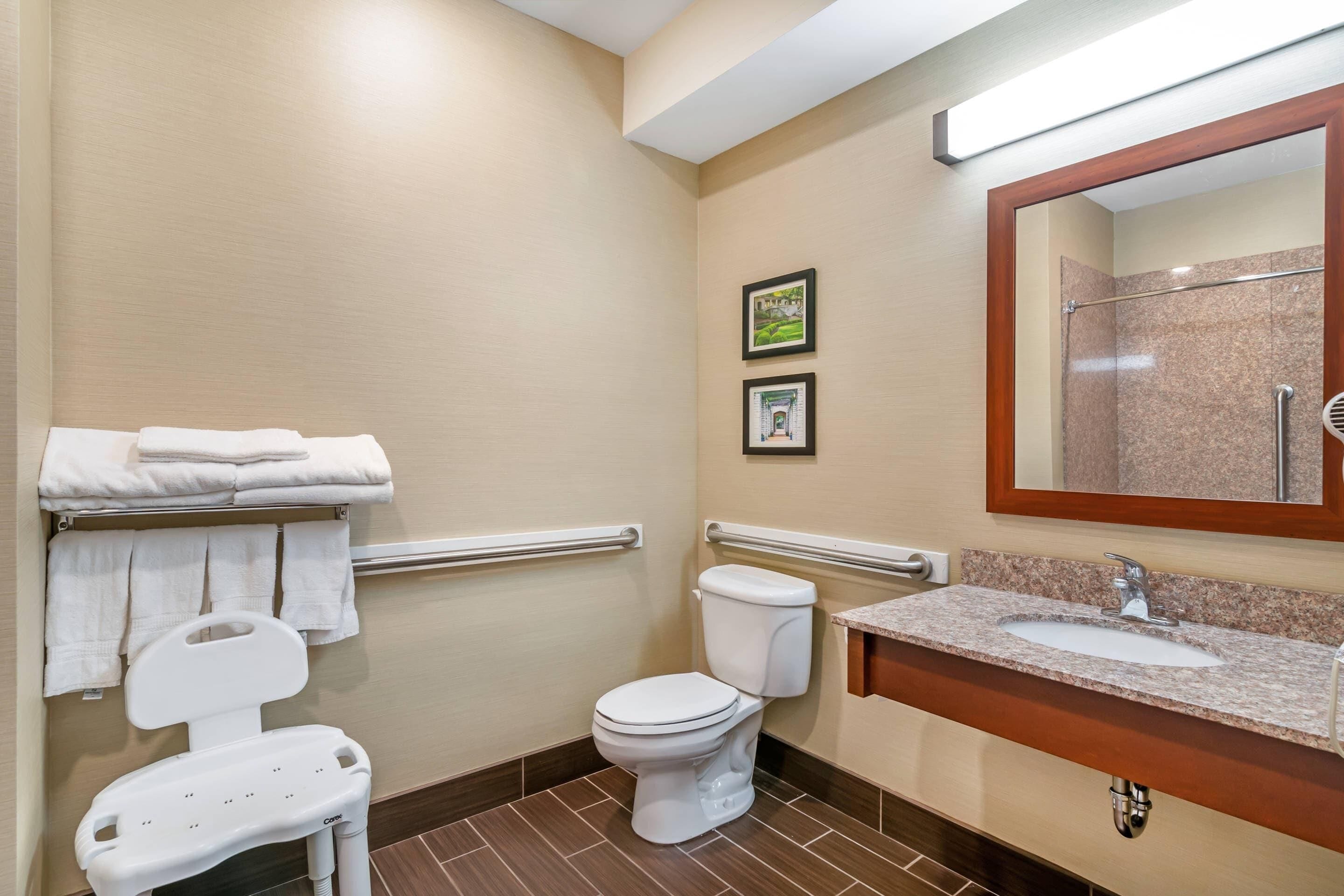 Un baño pequeño con inodoro, lavabo, espejo y barra de apoyo.