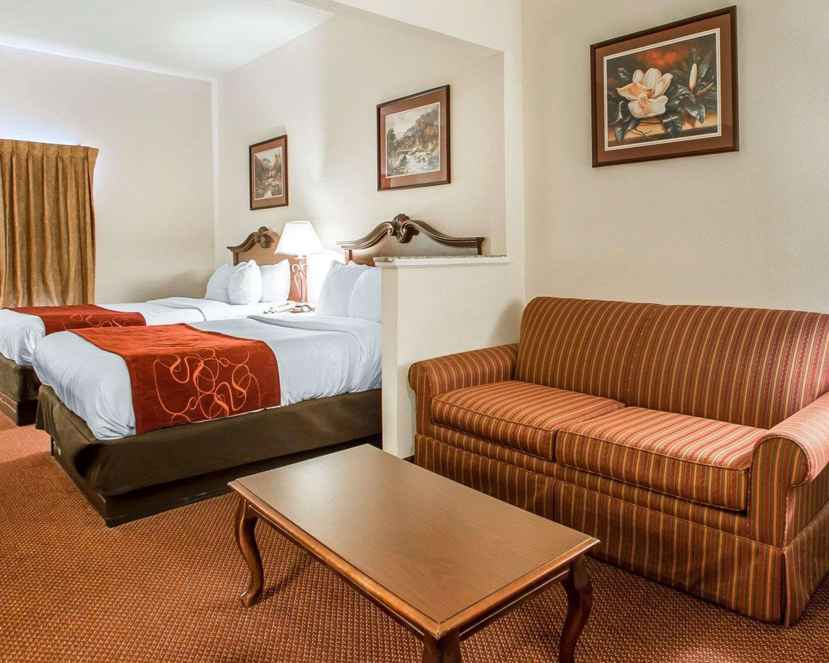 A hotel room with two beds, a sofa, a table, and framed artwork on the walls.