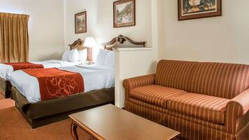 A hotel room with two beds, a sofa, a table, and framed artwork on the walls.