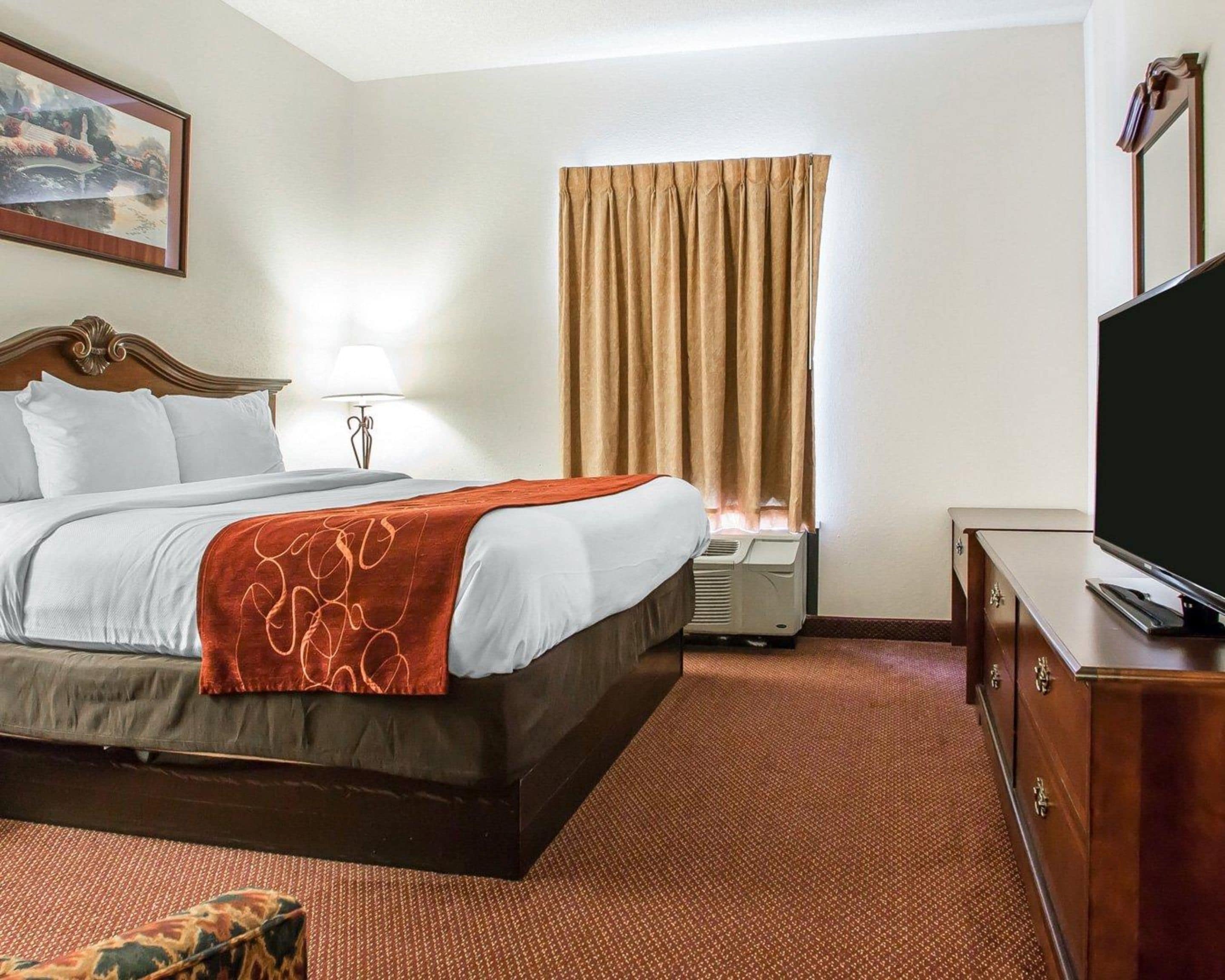 A hotel room with a bed, a television, a dresser, and a window with curtains.