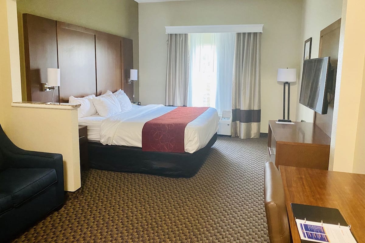 A hotel room with a bed, a desk, a chair, a television, and a window with curtains.