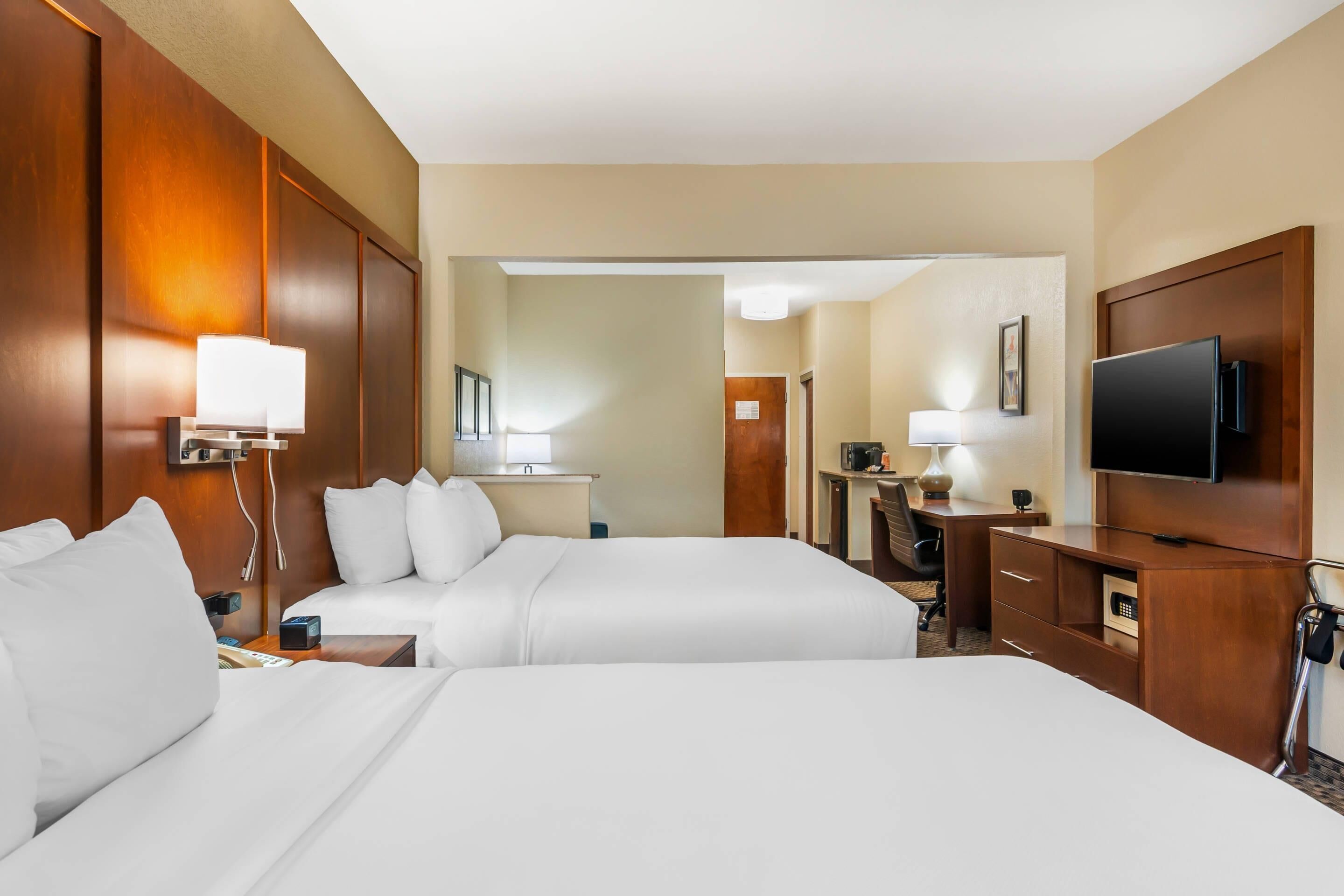 Ein Hotelzimmer mit zwei Betten, einem Schreibtisch, einem Fernseher und einem durch eine offene Tür einsehbaren Badezimmer.