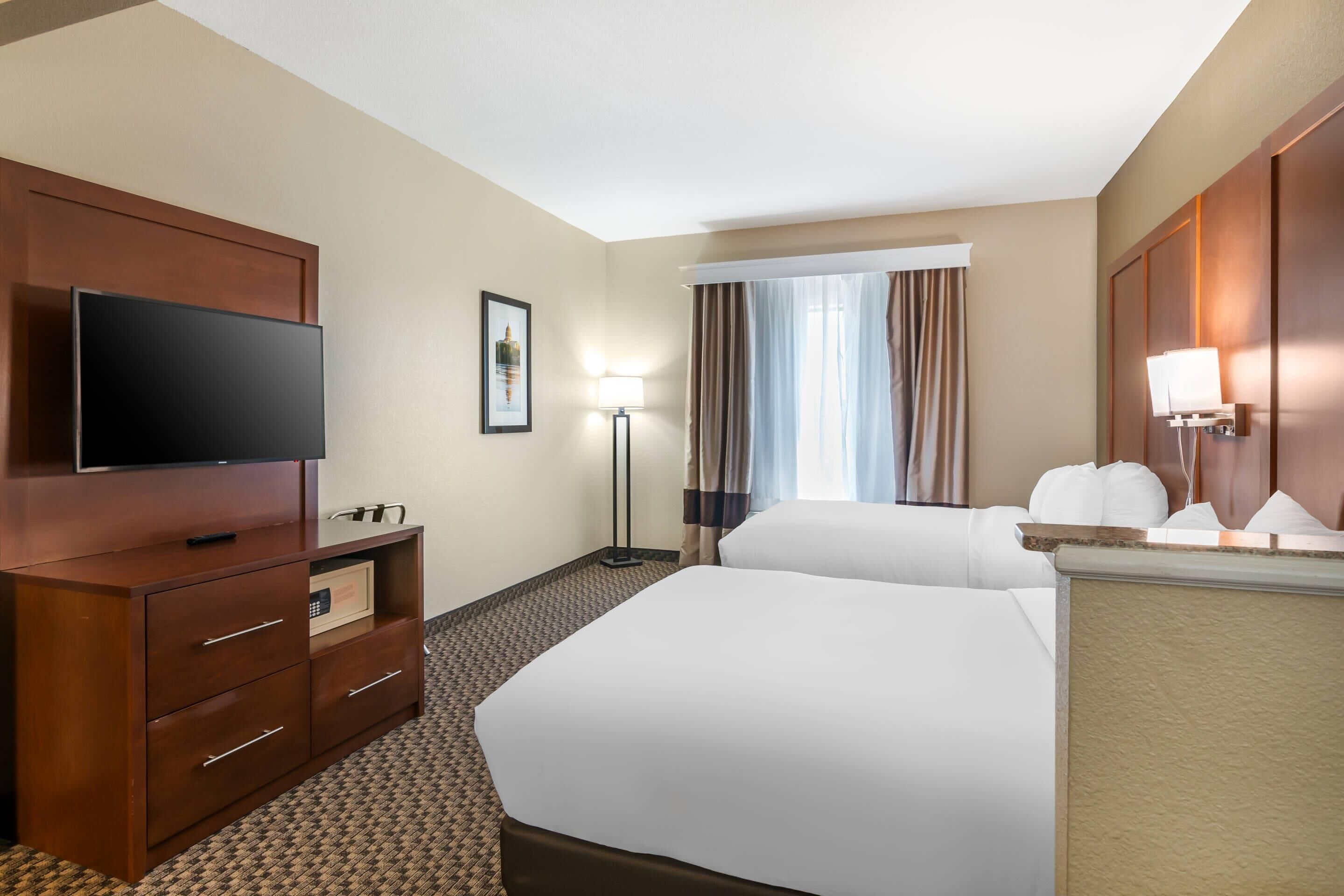 Ein Hotelzimmer mit zwei Betten, einem Fernseher, einem Schreibtisch und einer Lampe.