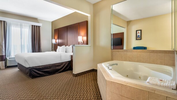 Habitación de hotel con una cama grande, zona de estar separada, baño con bañera y un espejo amplio.