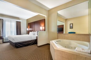 A hotel room with a large bed, a separate sitting area, a bathroom with a bathtub, and a large mirror. - Comfort Suites Jefferson City (Jefferson City)