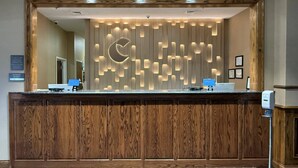Un mostrador de recepción con diseño de panel de madera, un espejo grande encima y un dispensador de tarjetas electrónicas a la derecha.