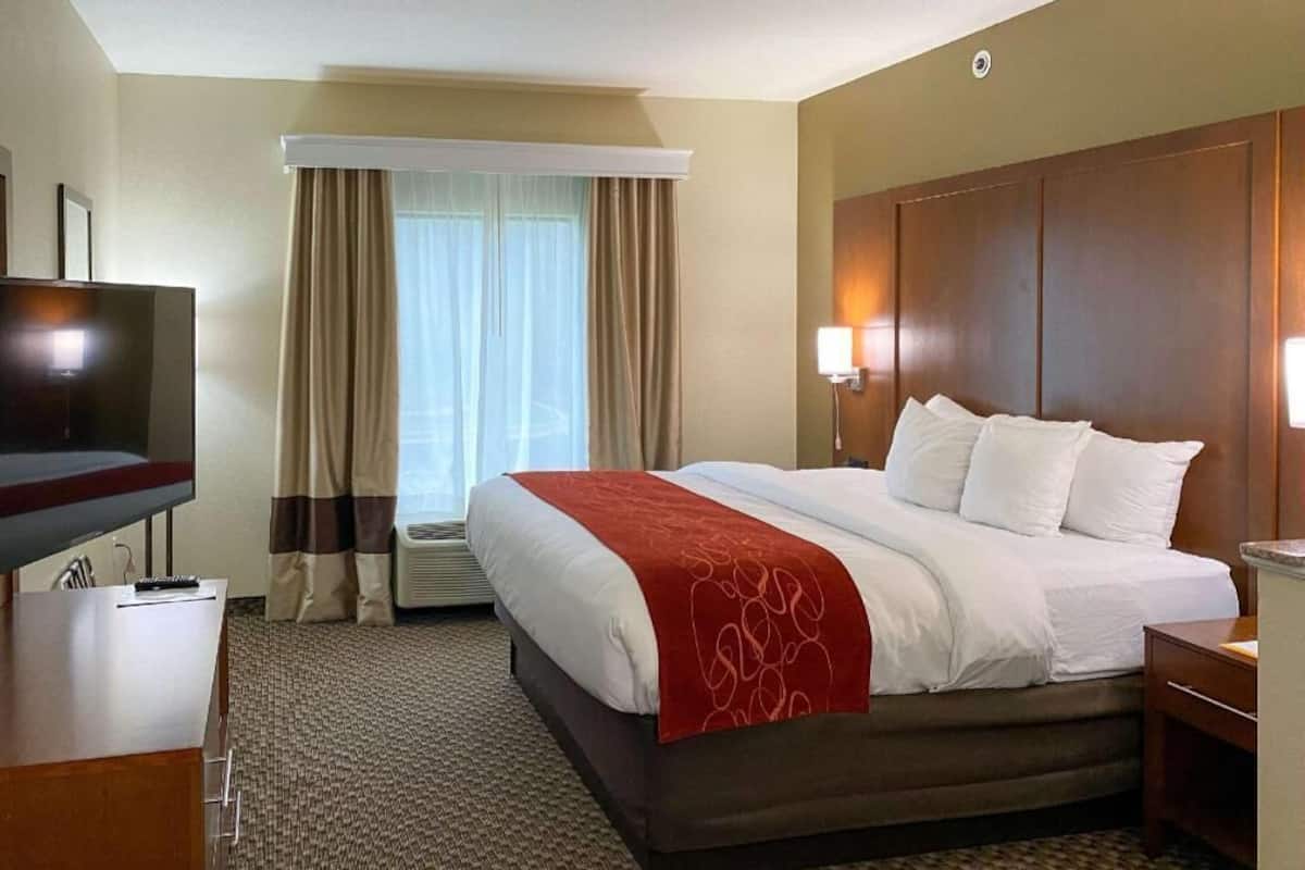 A hotel room with a bed, a TV, a desk, and a window with curtains.