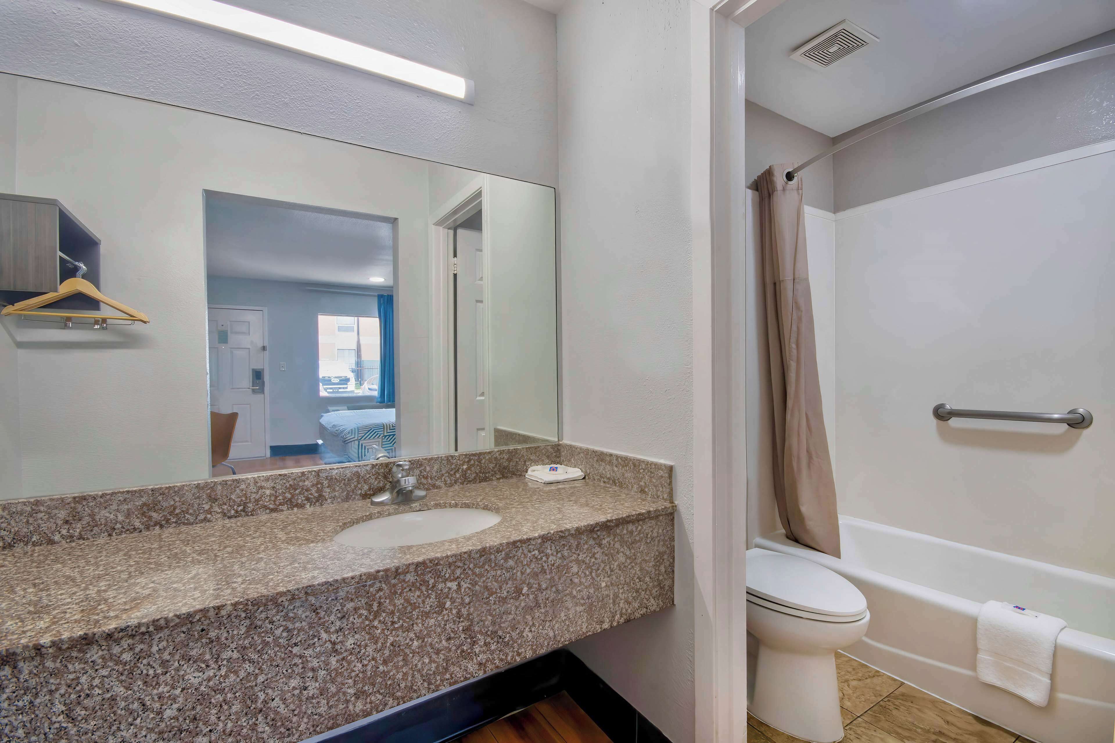 A bathroom with a granite countertop sink, a mirror, a toilet, and a bathtub.