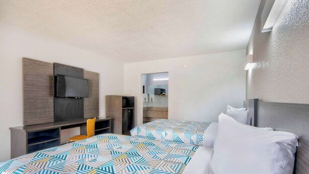 A hotel room with a bed, a desk, a chair, a TV, and a wardrobe. - Motel 6 Sulphur, LA (Sulphur)