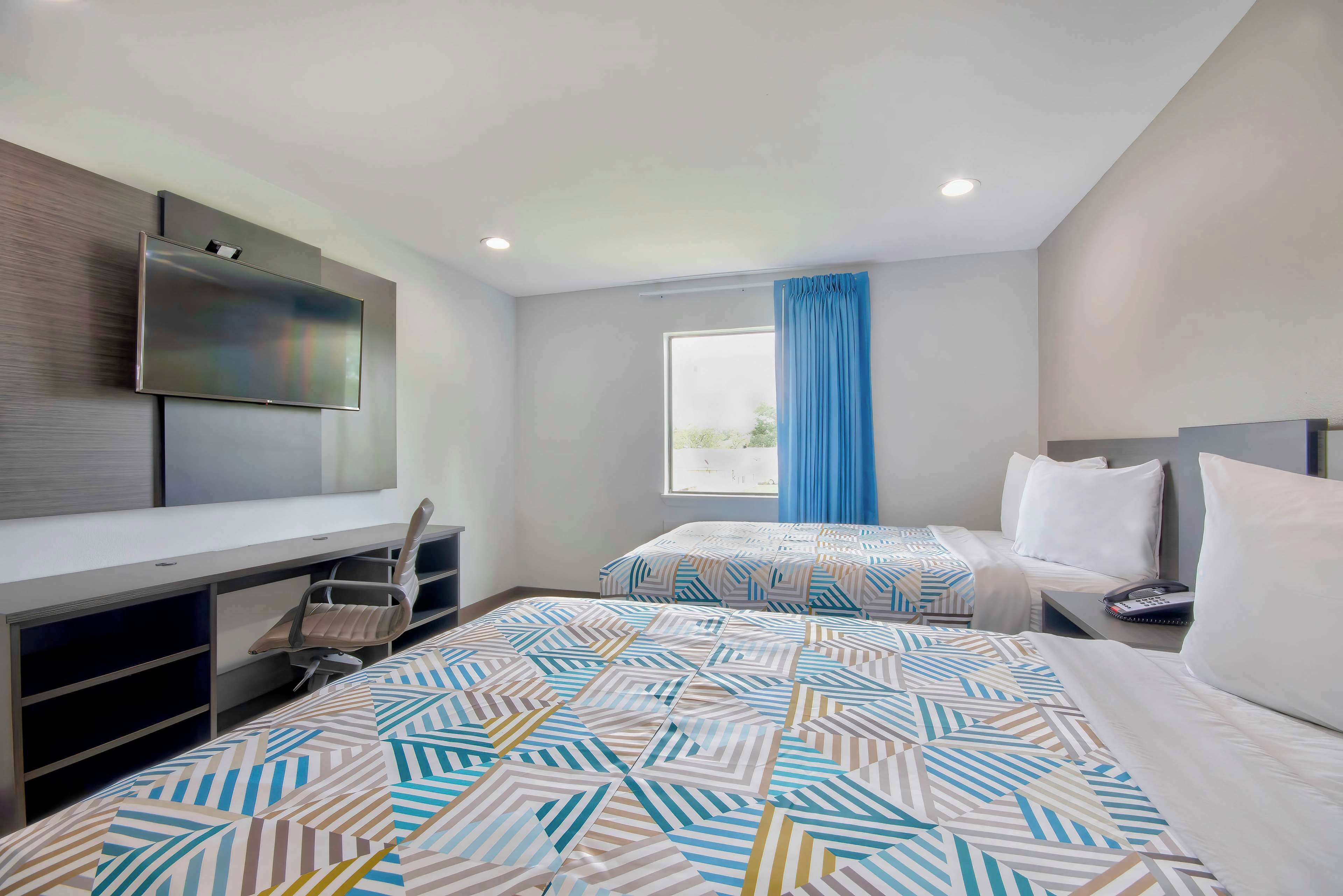 Une chambre d’hôtel avec deux lits, un bureau, une télévision et une fenêtre avec des rideaux.