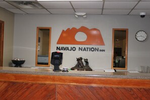 A reception desk with a sign reading "Navajo Nation Inn," a security camera, a clock, and a statue of a bear.