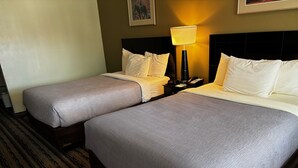 Een hotelkamer met twee bedden, een nachtkastje met een lamp en een ingelijste foto aan de muur.