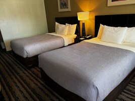 Habitación de hotel con dos camas, una mesita de noche con lámpara y un cuadro en la pared.