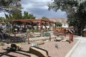 Un jardín desértico con una pérgola de madera, un pequeño arroyo y cactus.