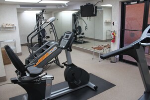 Un gimnasio con máquinas de cardio, un espejo y un extintor.